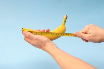 Hands measuring banana with measuring yellow tape on blue background