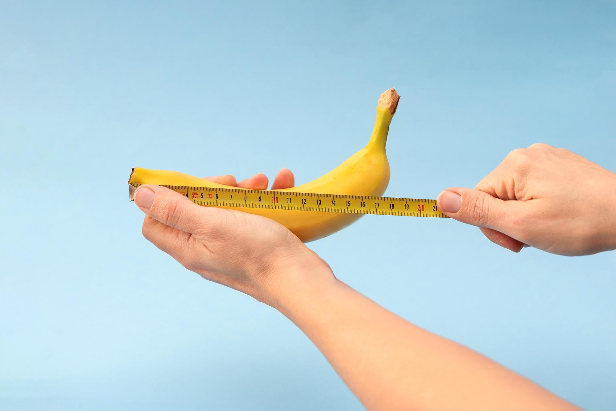 Hands measuring banana with measuring yellow tape on blue background
