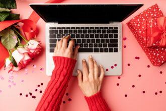 Valentines Day concept. Female hands typing on the keyboard, top view on pink background. Top view o