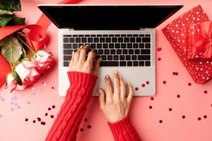 Valentines Day concept. Female hands typing on the keyboard, top view on pink background. Top view o