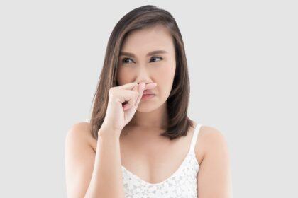 Asian woman in white dress catch her nose because of a bad smell against gray background