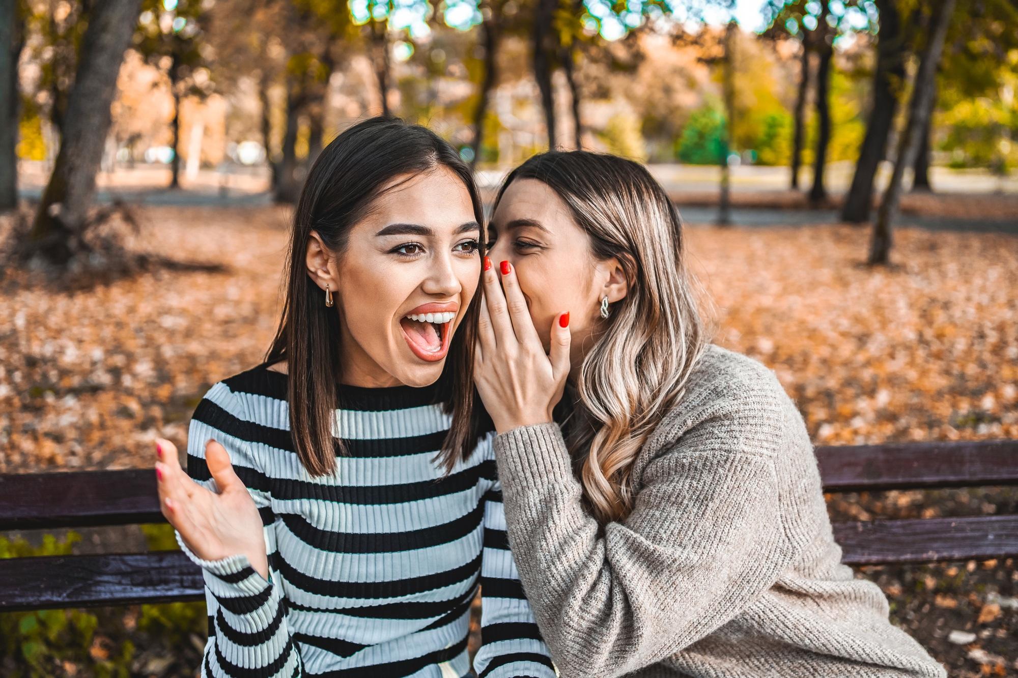 Two women whisper a secret in each other's ear and share a laugh