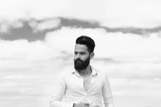 Portrait of an adult man smiling in front of a metal shutter.