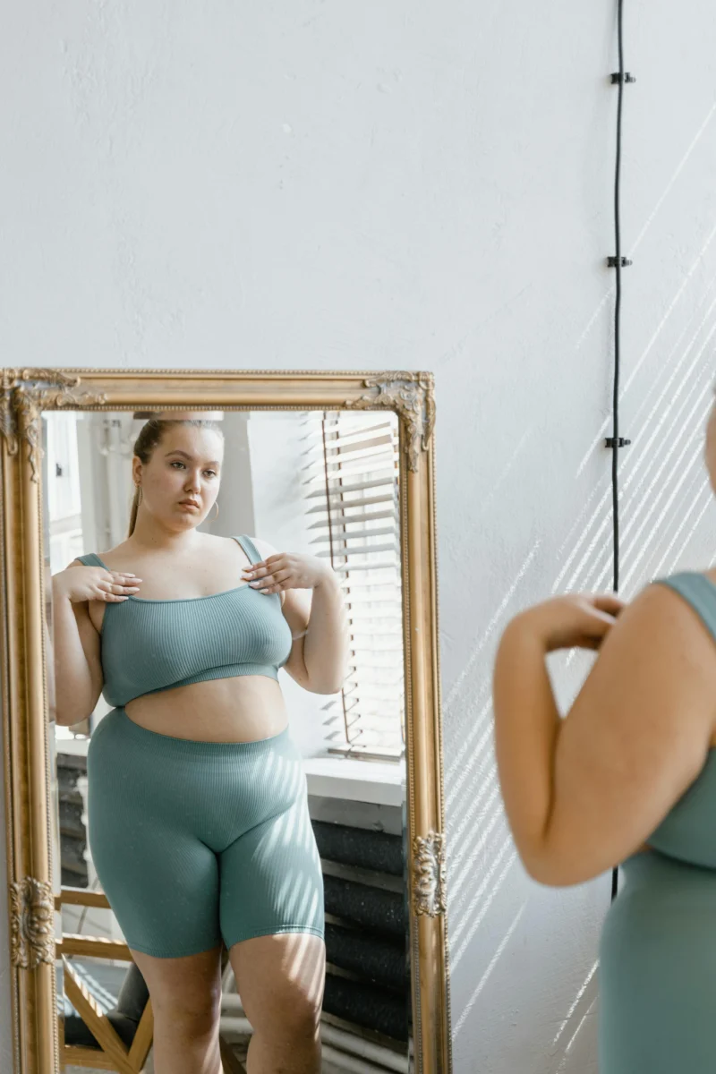 Confident plus size woman in sportswear looking at her reflection in a mirror indoors.