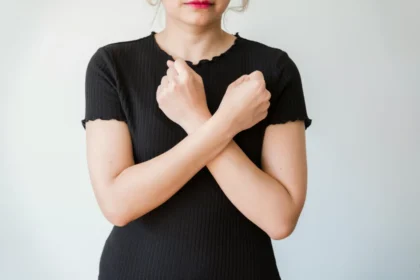 A woman in a black shirt crossing her arms in front of a plain white background.