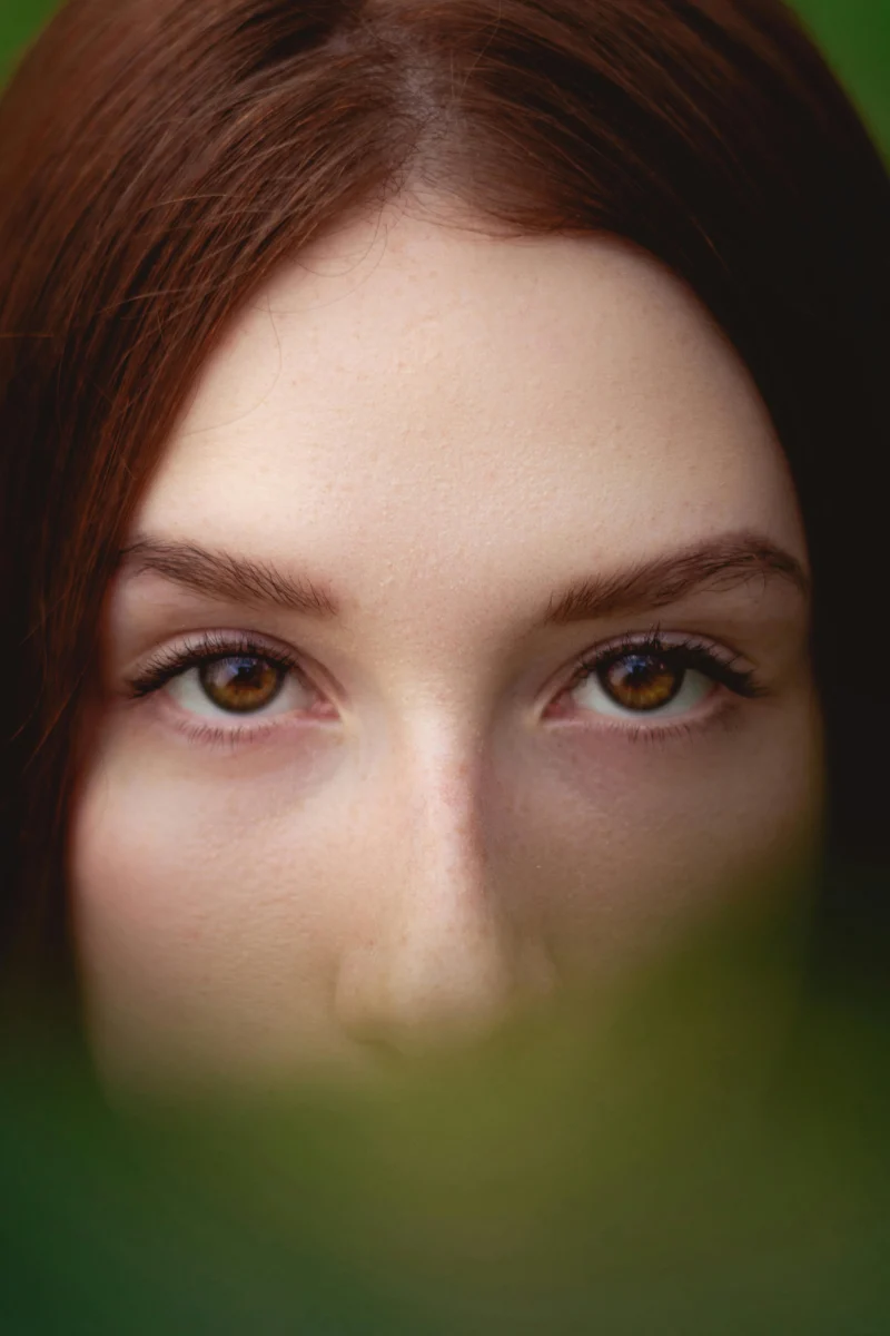 A captivating close-up of a woman's brown eyes partially obscured by foliage.