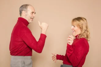 Elderly couple dancing joyfully in matching red outfits against a neutral background.