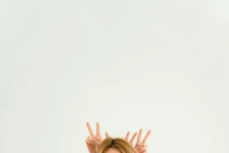 Woman in brown dress with peace sign gesture on white background, playful and charming.