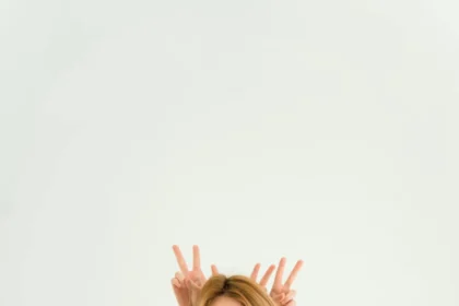 Woman in brown dress with peace sign gesture on white background, playful and charming.