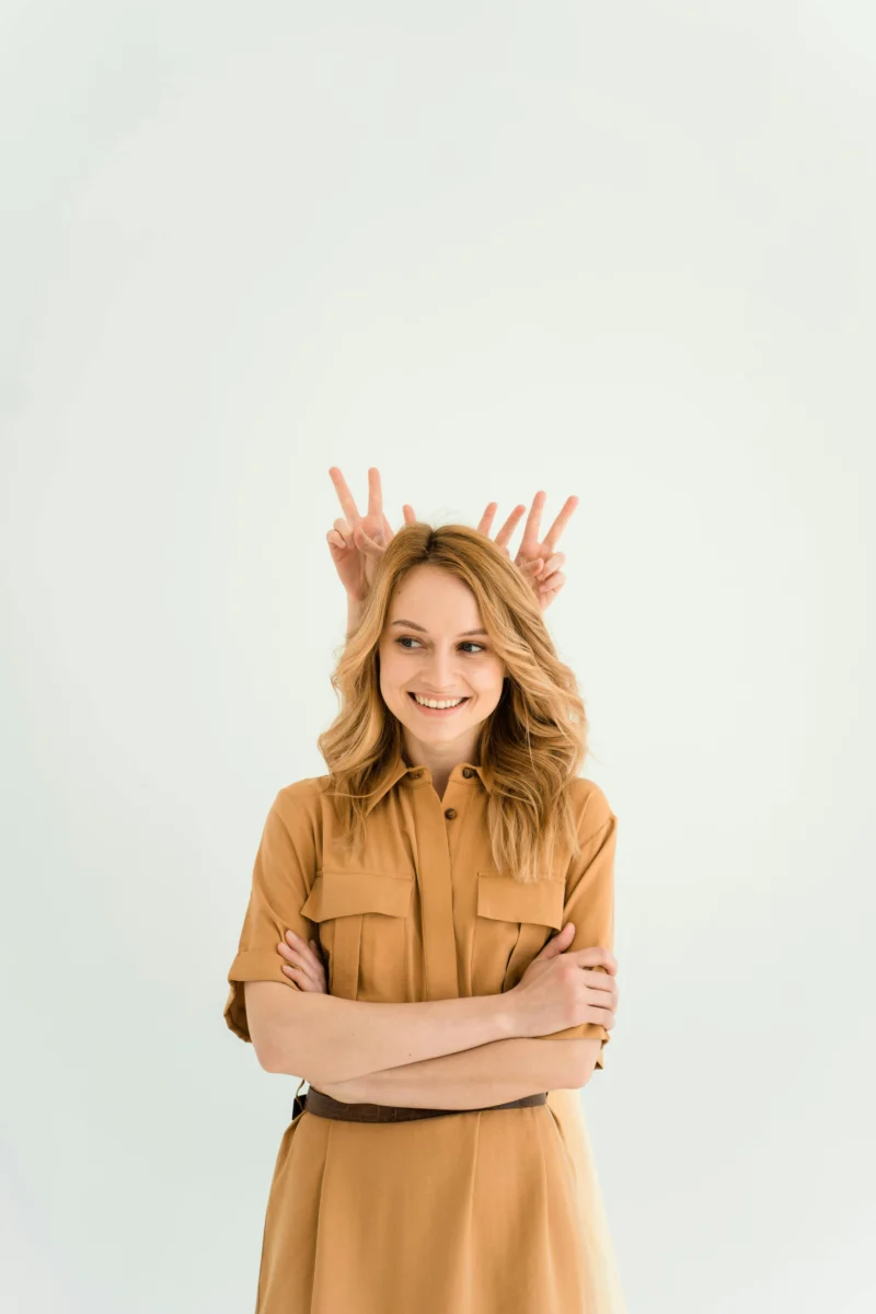 Woman in brown dress with peace sign gesture on white background, playful and charming.