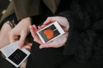 From above of anonymous couple in warm outerwear sitting with photos of heart shaped candy and romantic inscription during date