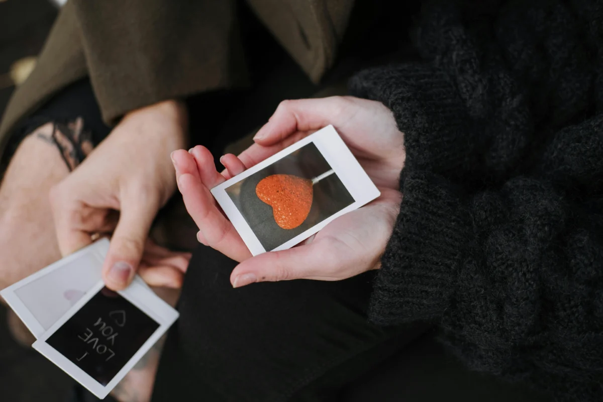 From above of anonymous couple in warm outerwear sitting with photos of heart shaped candy and romantic inscription during date