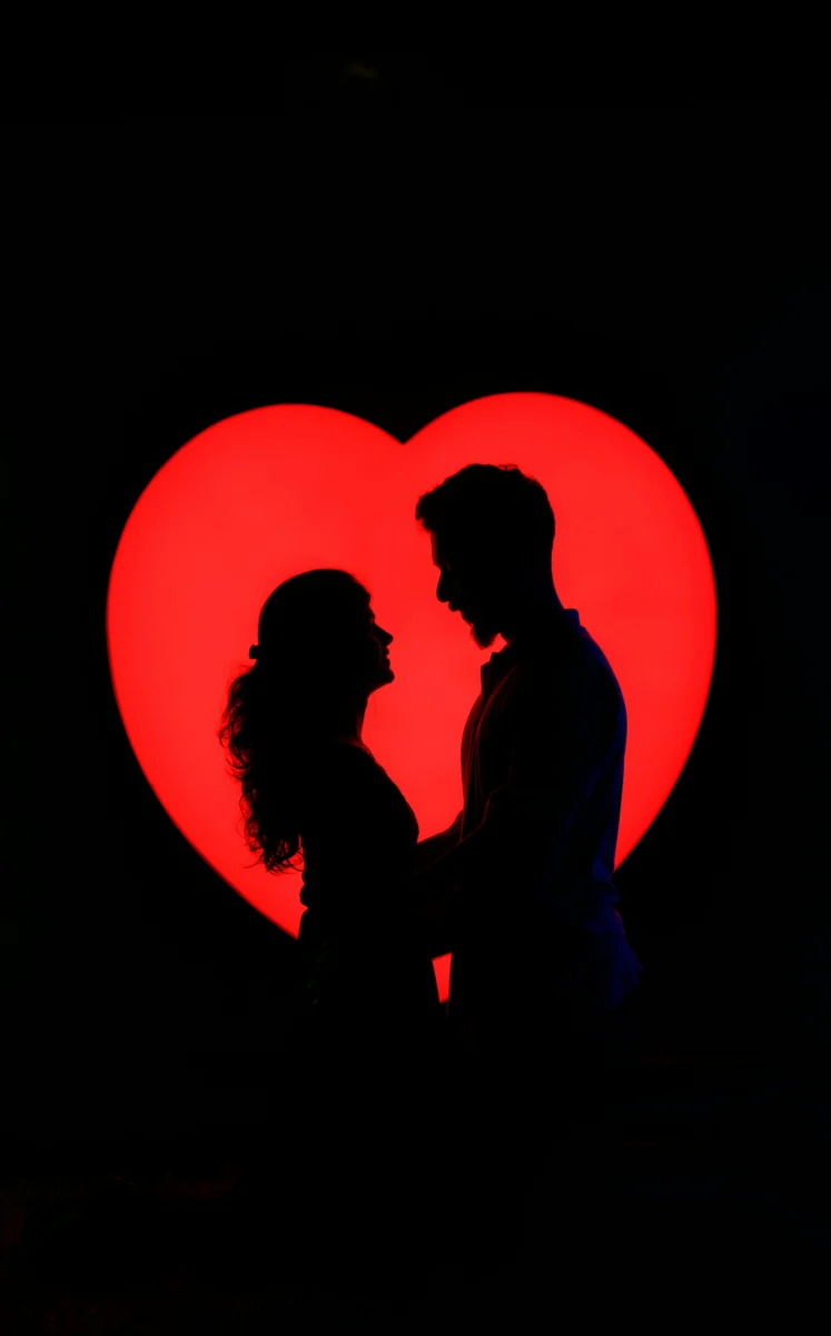Silhouette of a loving couple embracing against a vibrant heart backdrop.