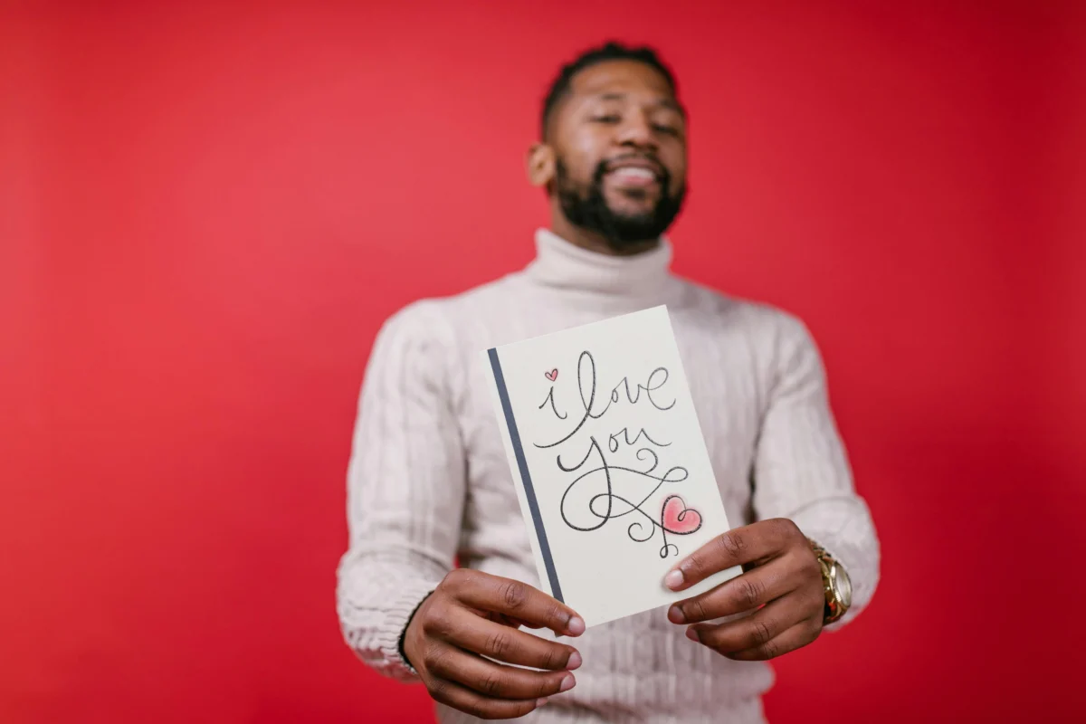 Smiling man holding an 'I love you' card on a vibrant red background, perfect for Valentine's Day themes.