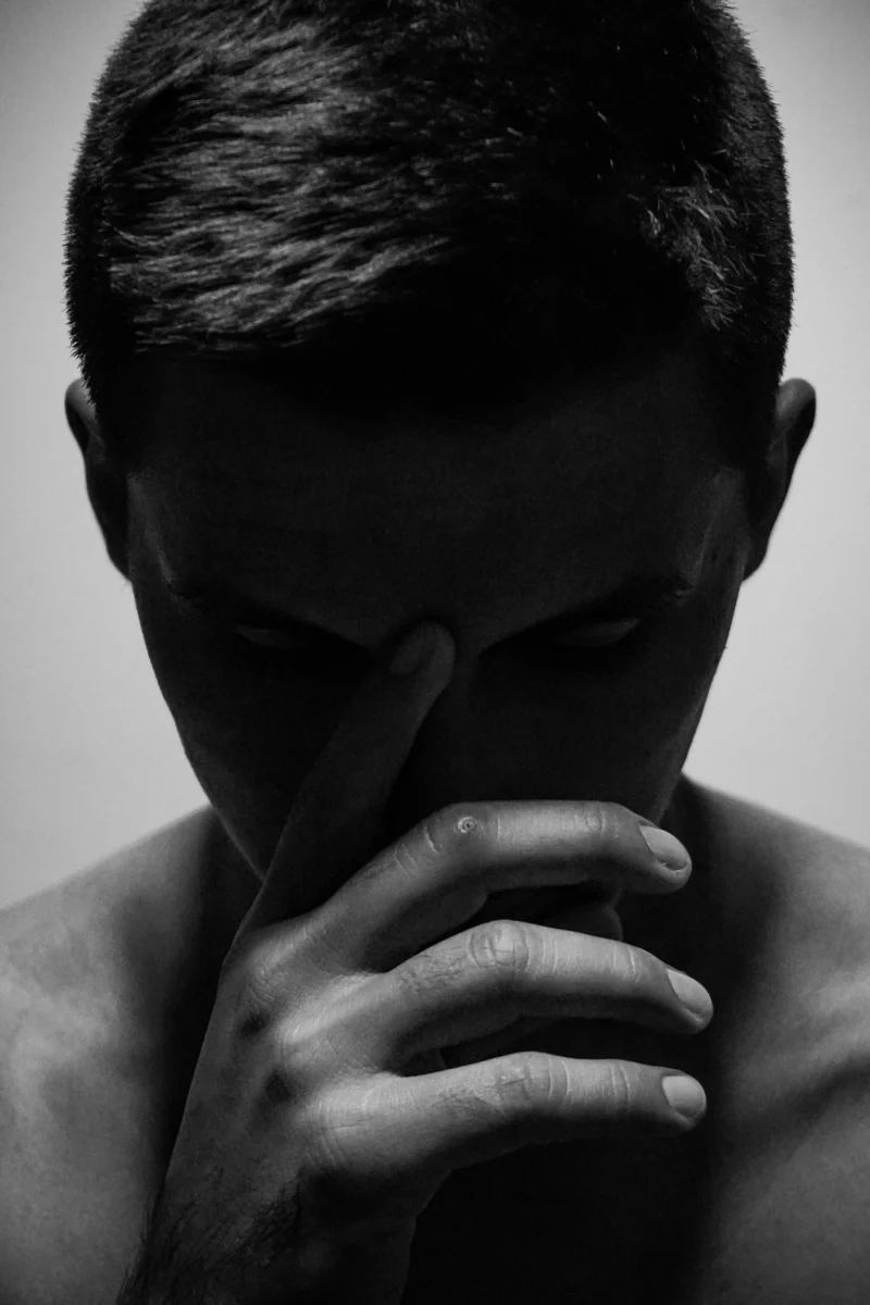 A dramatic black and white portrait of a shirtless man in a pensive pose, conveying deep thought.