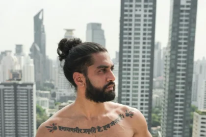 Tattooed man gazing over a cityscape from a rooftop, showcasing muscular physique and urban style.
