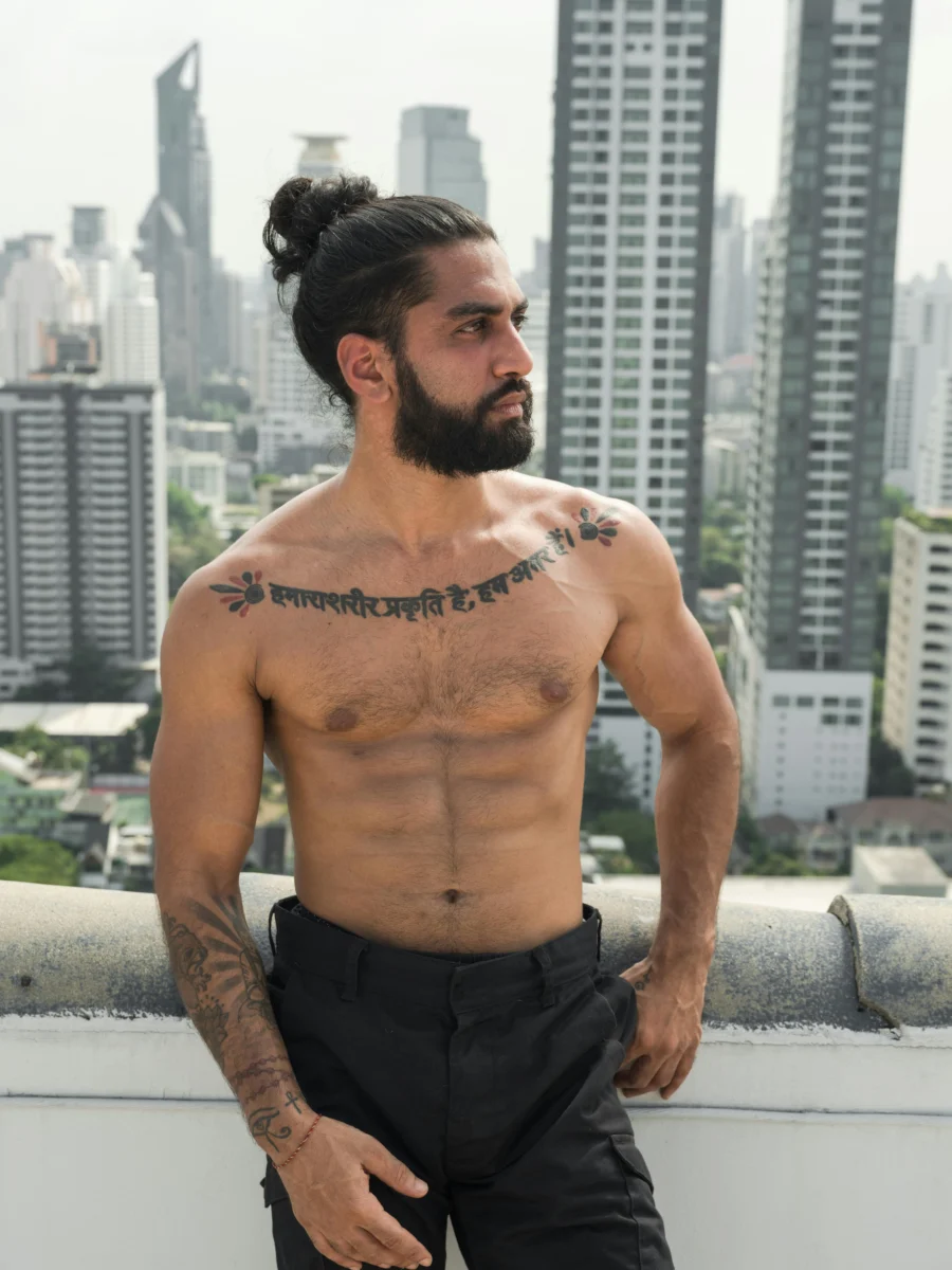 Tattooed man gazing over a cityscape from a rooftop, showcasing muscular physique and urban style.