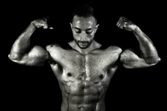 Black and white photo of a muscular male bodybuilder flexing his biceps in a dramatic pose.