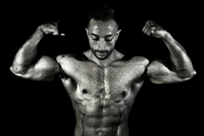 Black and white photo of a muscular male bodybuilder flexing his biceps in a dramatic pose.