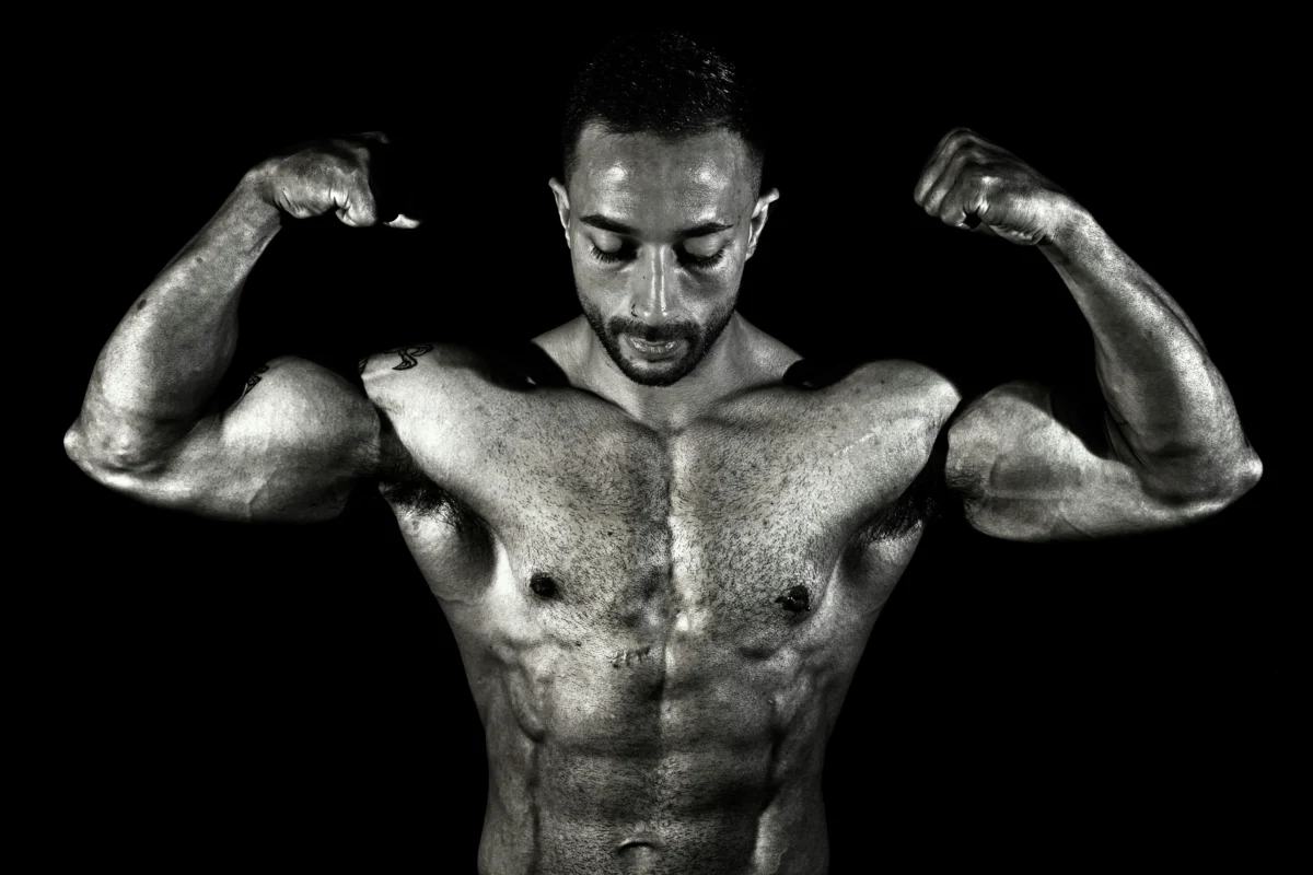 Black and white photo of a muscular male bodybuilder flexing his biceps in a dramatic pose.