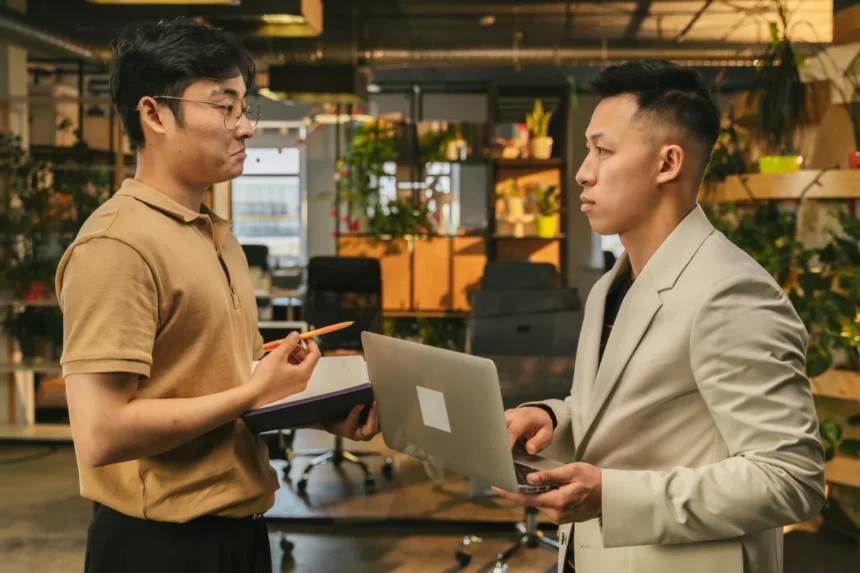 Two young men engaged in a discussion, collaborating on a project in a modern office setting.