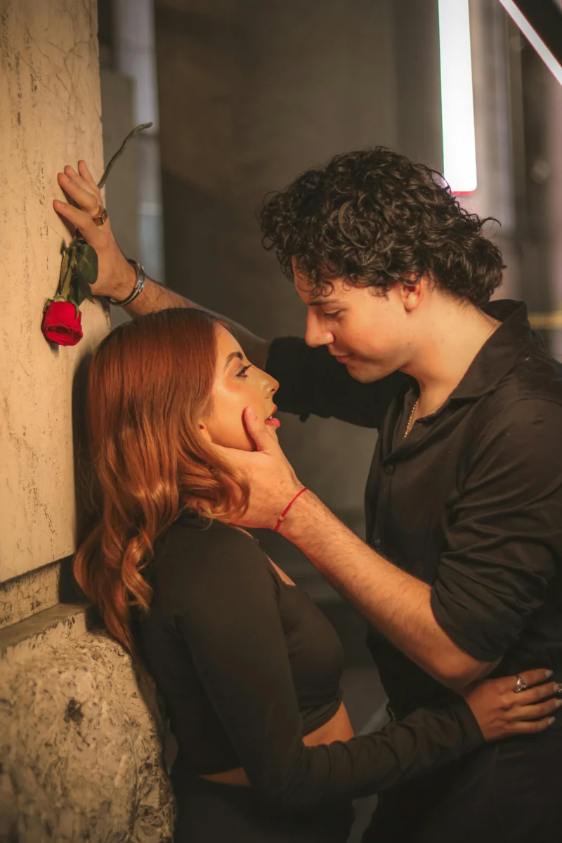 A couple romantically embracing on a city street at night with a red rose.