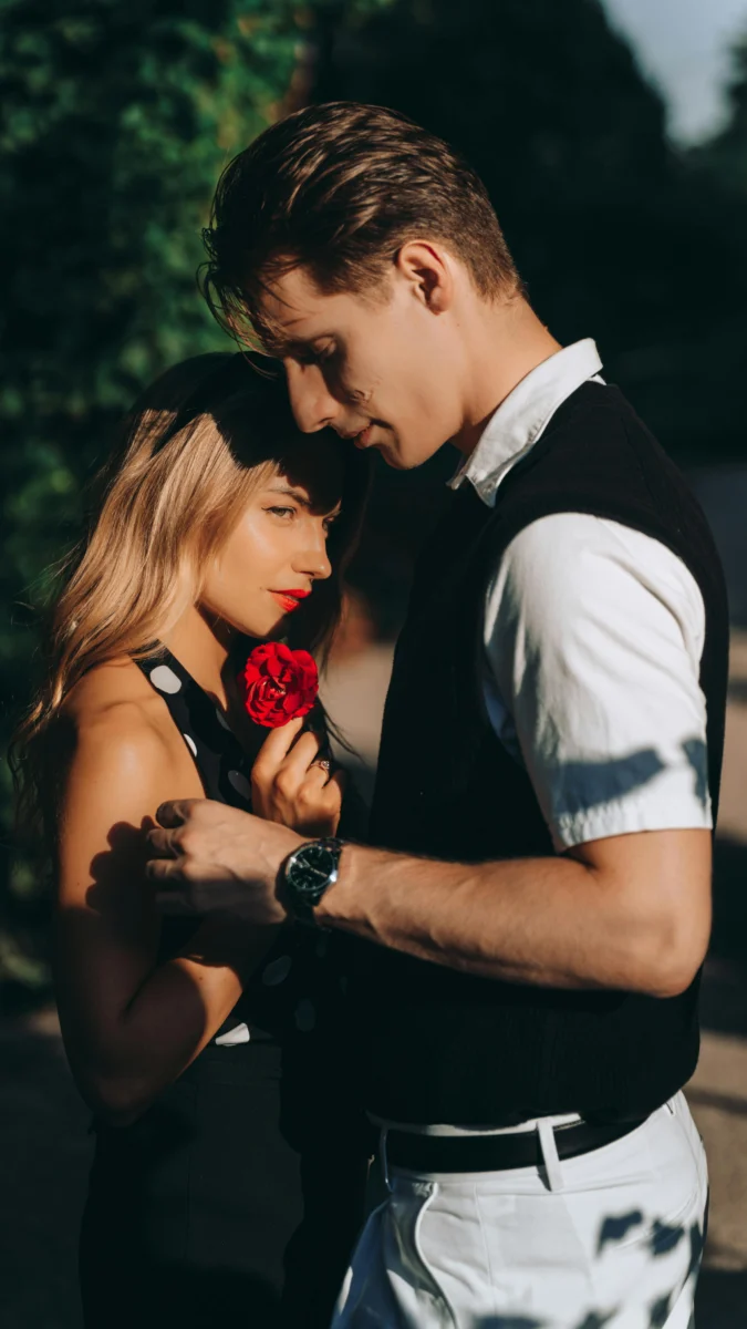 A romantic couple embracing outdoors, sharing a tender moment with a red rose.