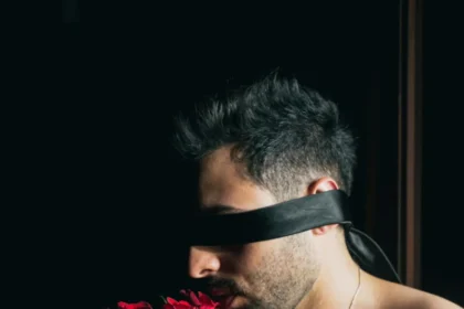 A blindfolded man holding a vibrant red rose bouquet, evoking a sense of mystery and sensuality.
