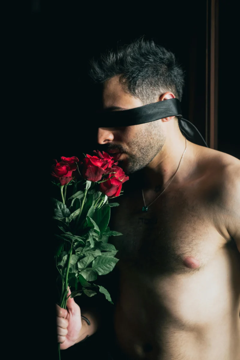 A blindfolded man holding a vibrant red rose bouquet, evoking a sense of mystery and sensuality.