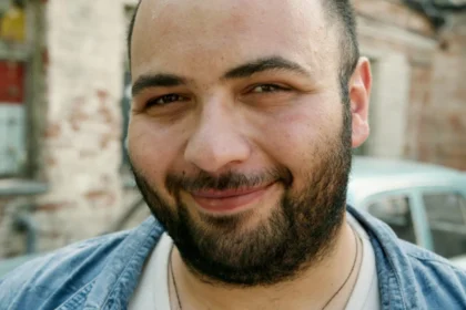 Close-up portrait of a smiling man with a beard outdoors.