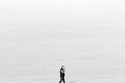 Black and white image of a lone walker in an expansive field, emphasizing solitude and minimalism.