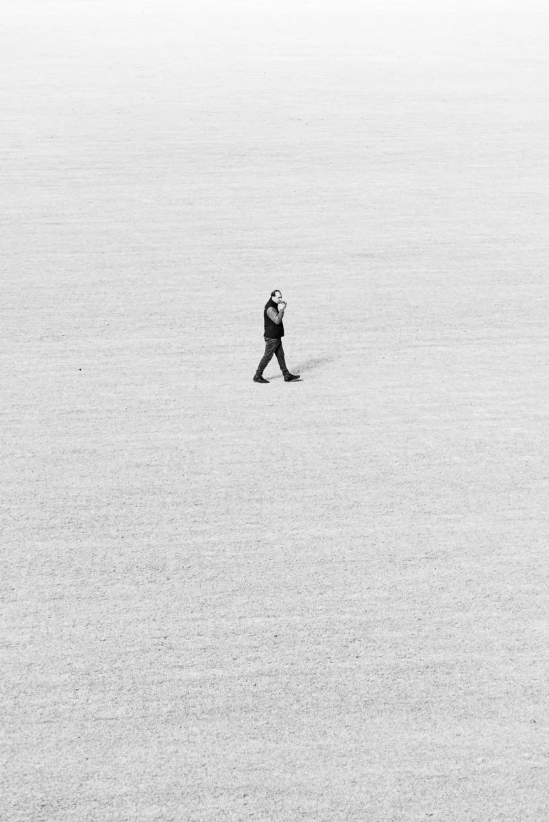 Black and white image of a lone walker in an expansive field, emphasizing solitude and minimalism.