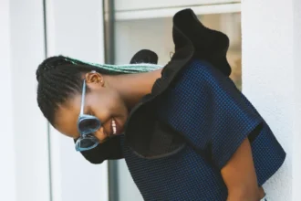 Fashion-forward woman smiling in blue knit top and sunglasses, holding a bag.