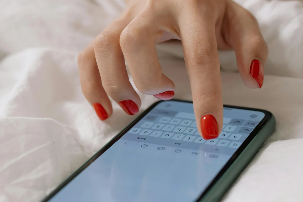 A close-up view of a woman's manicured hand typing on a smartphone, indoors.