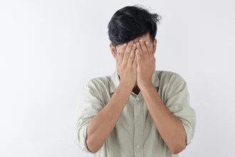 A man covering his face with hands, expressing feelings of stress and emotional struggle.