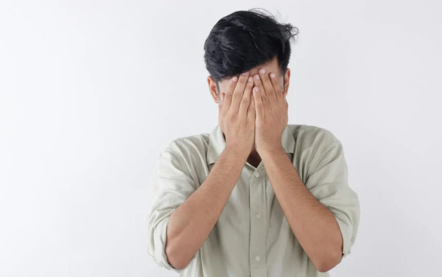 A man covering his face with hands, expressing feelings of stress and emotional struggle.