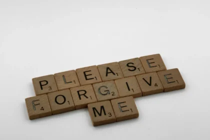 Wooden Scrabble tiles spelling 'Please Forgive Me' on a white surface, emphasizing forgiveness.