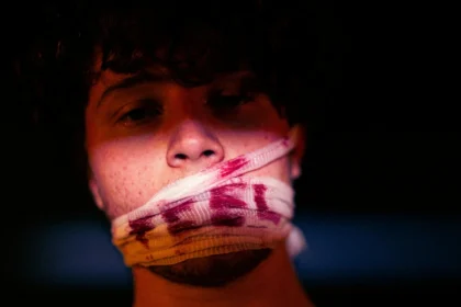 A moody portrait of a person with blood-stained bandage on mouth, symbolizing silence.